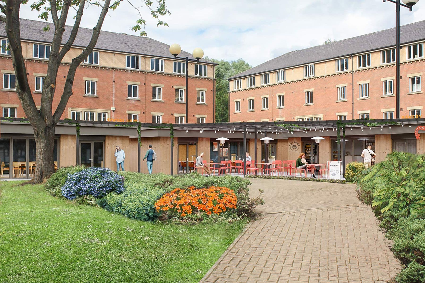 A photograph of The Leather Works courtyard featuring a green grass square with foliage and a path. The path leads to a wooden building with outdoor seating, with the larger accommodation building visible behind it.