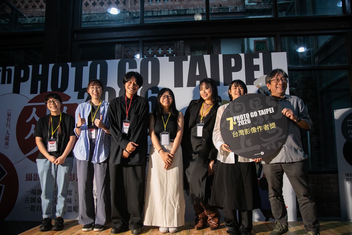 A group of people smiling on stage at a photography event. They hold a sign reading "Photo Go Taipei 2026" against a backdrop with similar text.