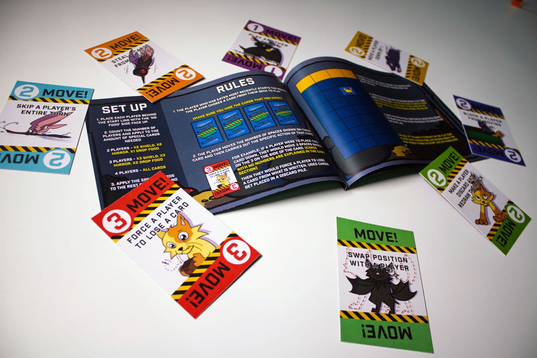 An image of a board game setup with an open rulebook and colourful cards scattered around, each featuring different animated characters and instructions.