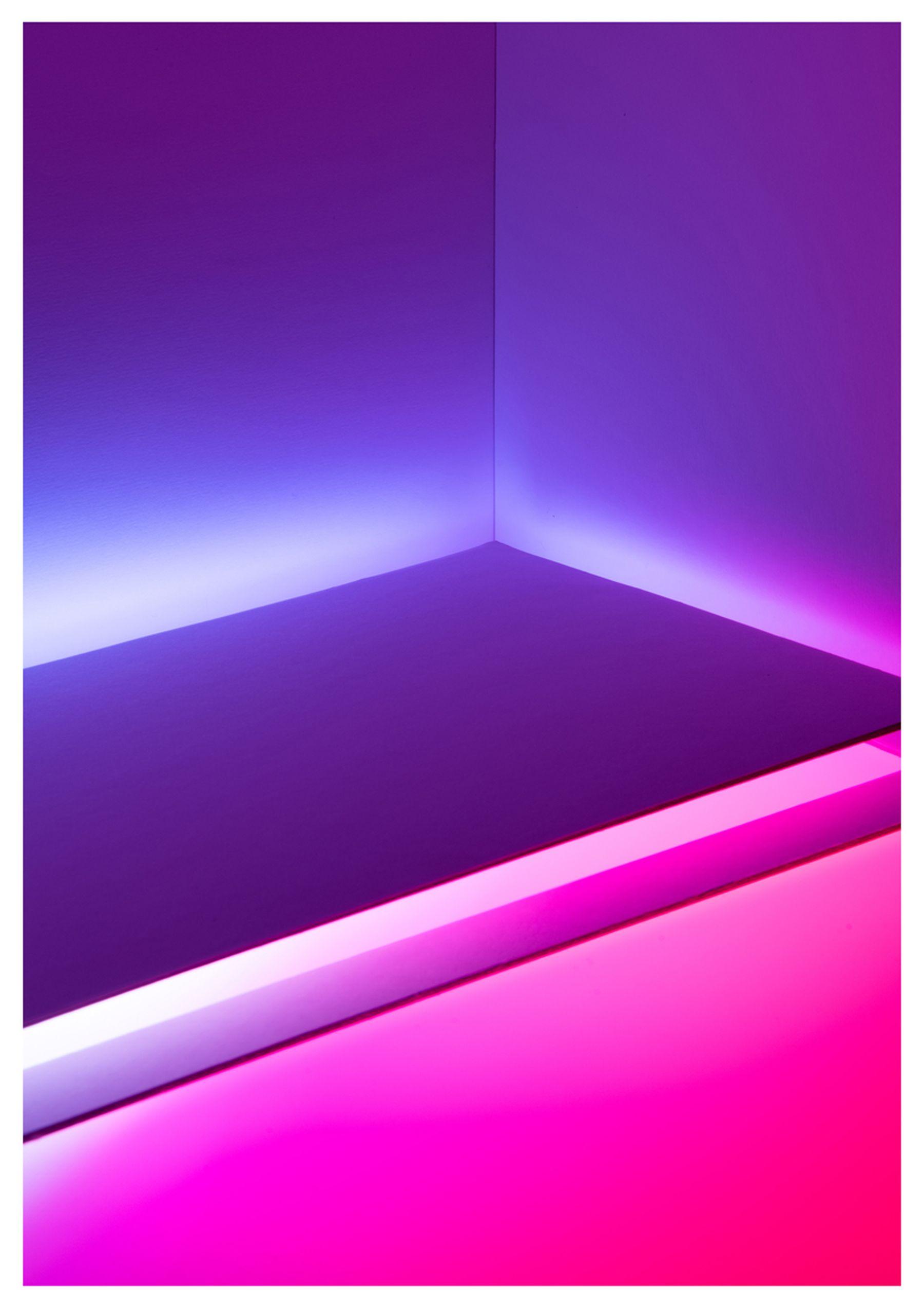 A photo of the corner of an indoor seat mounted against a wall. Part of the seat is purple and the bottom is coloured with pink lighting.