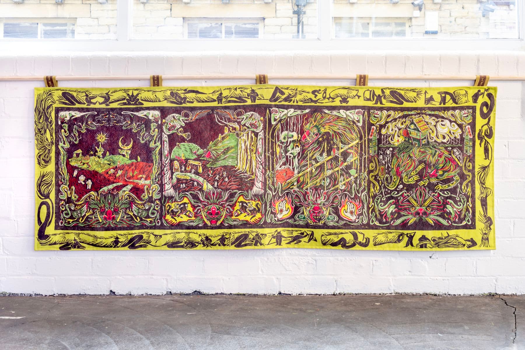 A vibrant, abstract tapestry with intricate patterns and vivid colors hangs on a white brick wall.