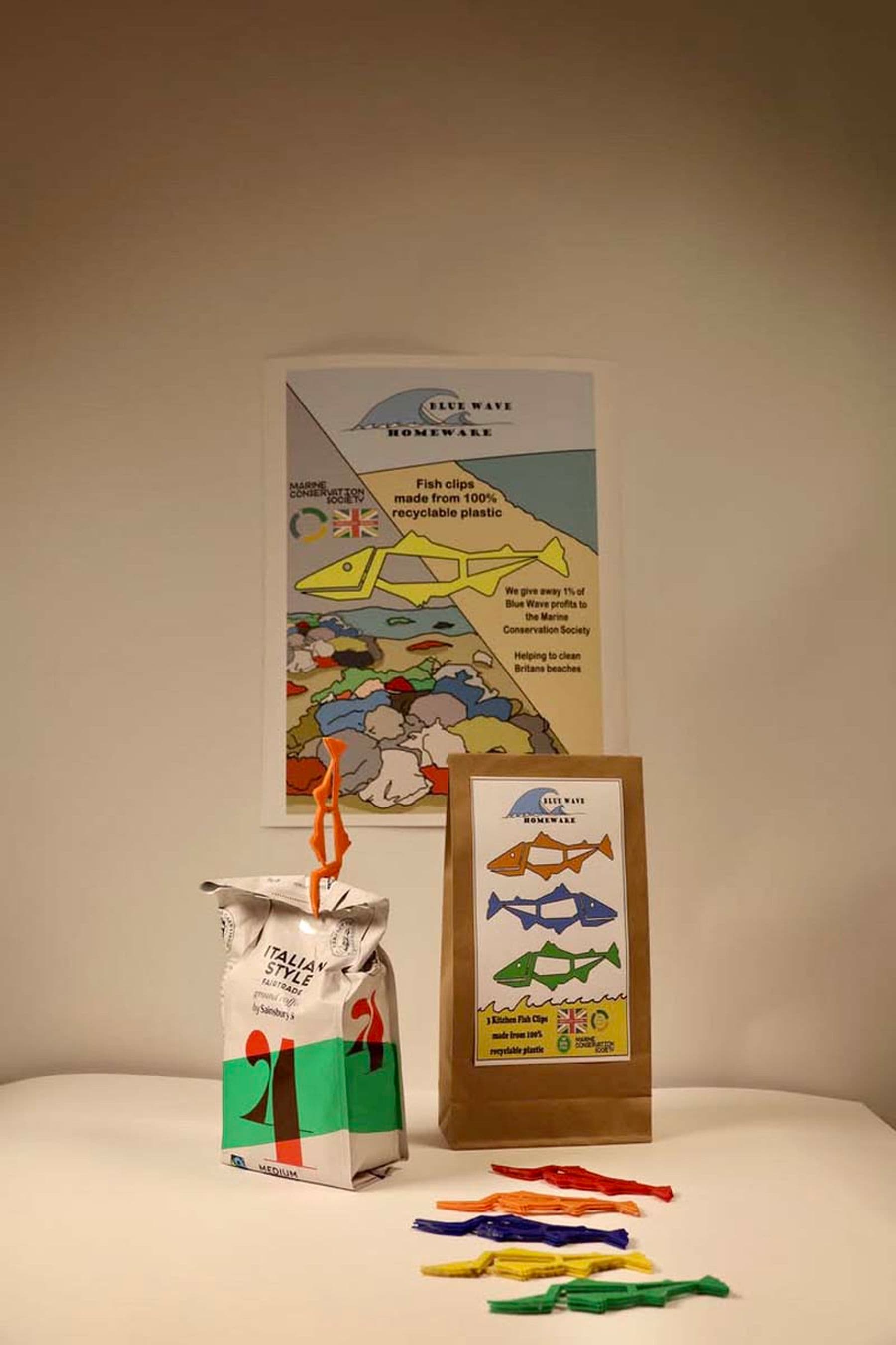A photograph of a packaging display with colourful fish-themed designs, including a poster, a paper bag, and scattered fish-shaped plastic strips on a table.