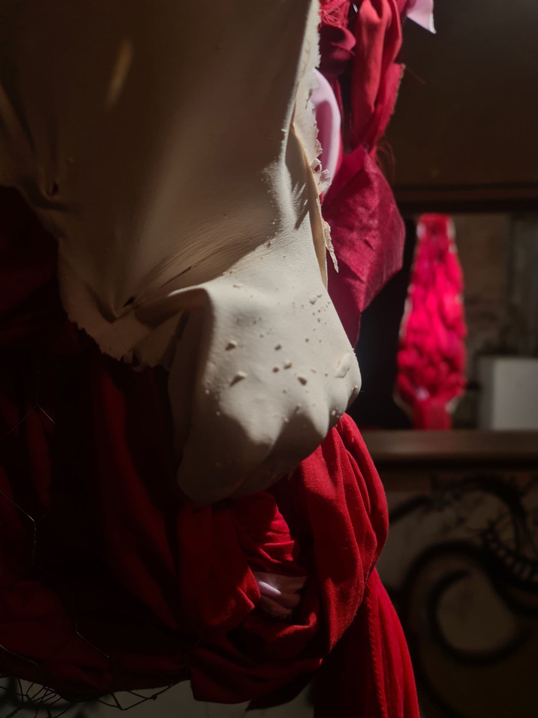 Close-up of a textured white sculpture with red fabric draped around it, set against a dimly lit background with a blurred reflection.
